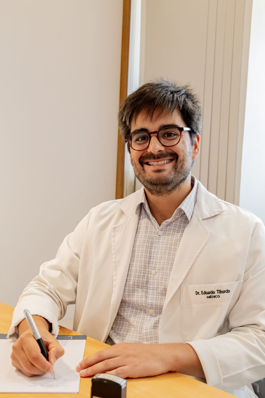 Dr. Eduardo Tiburcio, médico com pós-graduação em cuidados paliativos, escrevendo à mesa do consultório